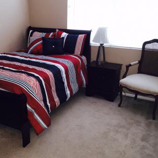 A cozy bedroom with a single bed featuring striped bedding, a nightstand with a lamp, and an armchair.