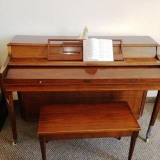 A wooden piano with a matching bench and an open music book on the stand.