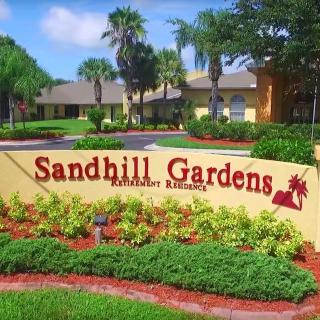 Entrance to Sandhill Gardens residential area with landscaped greenery and palm trees.