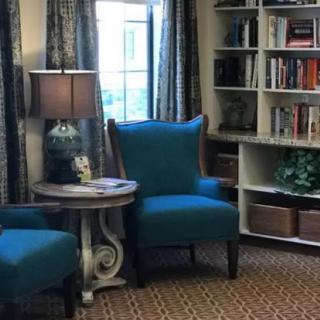 A cozy living room corner with blue armchairs, a lamp, and a bookshelf.