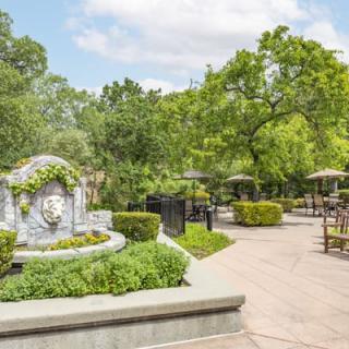 A serene garden with a decorative fountain and lush greenery, featuring benches and a winding pathway.
