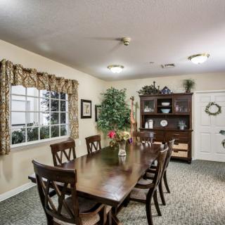 A well-furnished dining room with a long table, multiple chairs, and decorative elements like curtains and indoor plants.