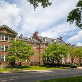 A scenic view of a brick residential building surrounded by trees under a partly cloudy sky.