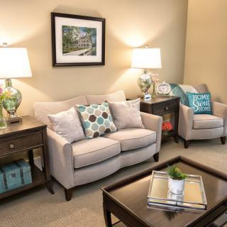 A cozy living room with a beige sofa and armchair, accented by colorful pillows and illuminated by matching table lamps.