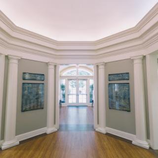 A beautifully designed interior hallway featuring elegant columns and artwork along the walls, leading to a bright entrance.