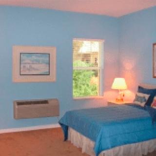 A cozy bedroom with blue walls, featuring a bed and a lamp by the window.