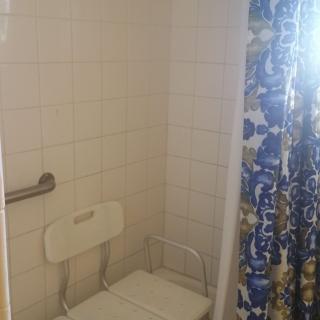 A bathroom with a shower area featuring a shower chair, grab bar, and a colorful curtain.