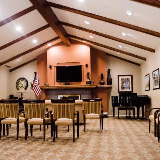 A spacious room with a beamed ceiling, featuring seating, a television, and a piano.