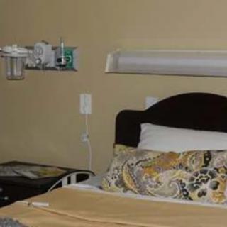 A hospital room with a neatly made bed and medical equipment on the wall.