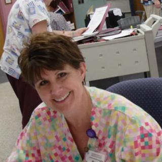 A smiling nurse sitting at a desk in an office setting.