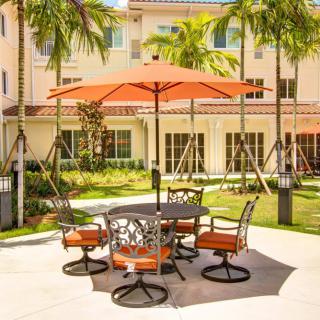 A sunny patio with an orange umbrella, surrounded by palm trees.