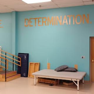 A bright therapy room featuring the word 'DETERMINATION' prominently displayed on the wall, symbolizing motivation and strength in rehabilitation.