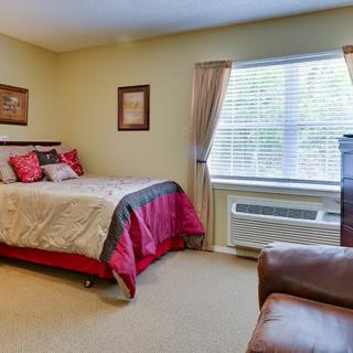 A cozy bedroom with a neatly made bed, window with curtains, and comfortable furnishings.