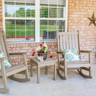 A cozy porch setup with two rocking chairs, a small table, and a flower pot against a brick wall.