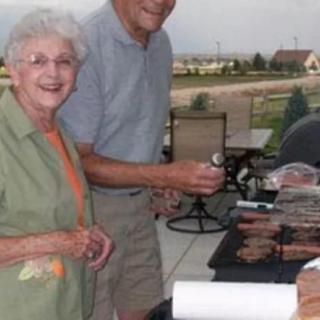 An elderly couple enjoying a barbecue outdoors, standing by the grill.