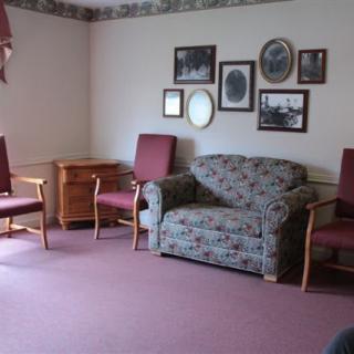 A vintage-style living room with a floral sofa, two chairs, and framed pictures on the wall.