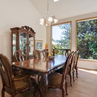 A spacious dining room with a wooden table, ornate chairs, and a chandelier, featuring large windows that allow natural light to fill the space.