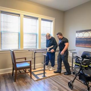An elderly person receiving assistance with physical therapy using parallel bars.