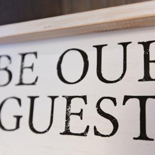A decorative sign with the phrase 'BE OUR GUEST' written on it.
