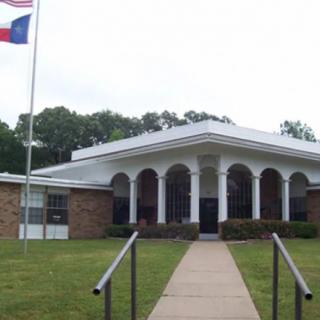 A school building with a flagpole in the front yard and a walkway leading to the entrance.