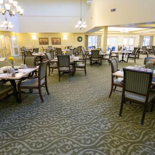 An elegant dining area with neatly arranged tables and chairs, featuring chandeliers and intricate carpet designs.