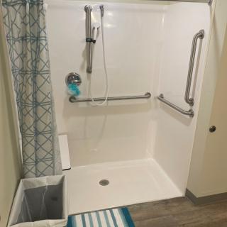 An accessible bathroom shower featuring grab bars and a patterned curtain.