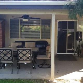 A cozy backyard patio with a table, chairs, and a ceiling fan.