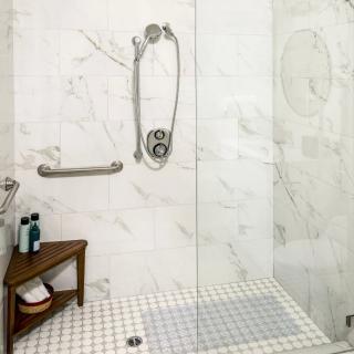 A modern shower with glass doors, marble tiles, and a small wooden bench.