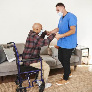 A caregiver assists an elderly person with mobility at home.