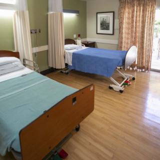 A well-lit hospital room with two beds and a wooden floor.