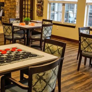 A cozy dining area featuring several tables and chairs with decorative table settings, set against a wooden floor and natural light streaming in through the windows.