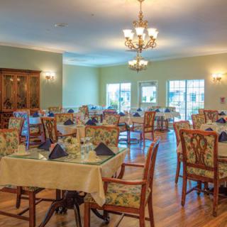 An elegant dining room with neatly arranged tables and chairs, featuring chandeliers and wooden flooring.