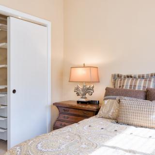 A cozy bedroom featuring a neatly made bed with decorative pillows and a warm bedside lamp next to a sliding closet door.
