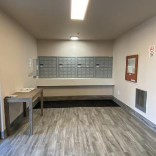 A modern mailroom with gray mailboxes, a table, and wood-style flooring.