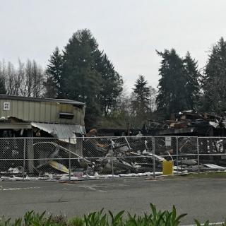 A view of a burnt-down building surrounded by fencing, with trees in the background.