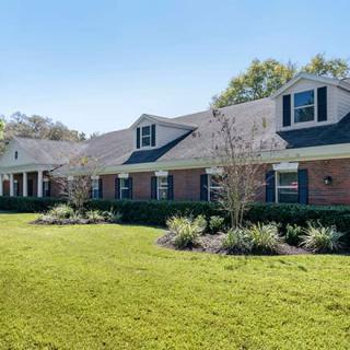 A large brick residential house with a well-maintained lawn and surrounding trees.