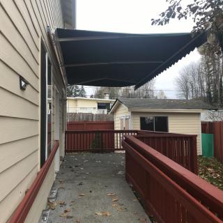 A house with a deck featuring an extended awning, surrounded by a red fence on an overcast day.