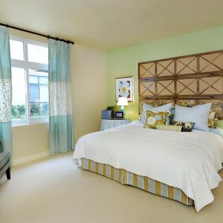 A cozy and well-decorated bedroom featuring a large bed with multiple pillows, soft lighting, and a window with light curtains.