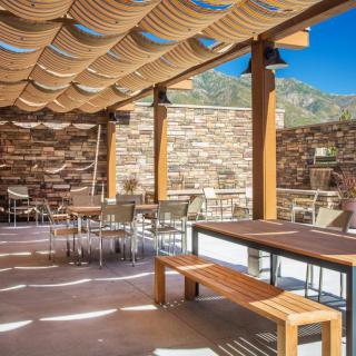 A spacious outdoor patio with wooden furniture and a pergola for shade, surrounded by stone walls on a sunny day.