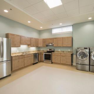 A modern kitchen with stainless steel appliances, wooden cabinets, and a laundry area.