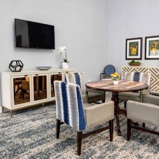 A modern living room featuring a stylish dining area with a wooden table and mixed fabric chairs, complemented by wall art and a mounted television.