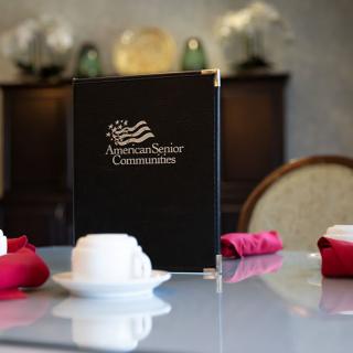 A dining table set with a menu and tea cups in an elegant restaurant setting.