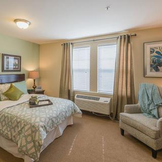 A cozy bedroom with a neatly made bed, an armchair, and softly lit lamps.
