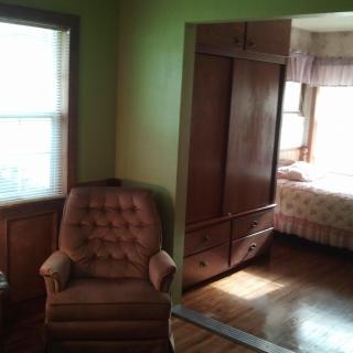 A cozy corner featuring a tufted armchair next to a window, with an adjoining bedroom visible through an open doorway.