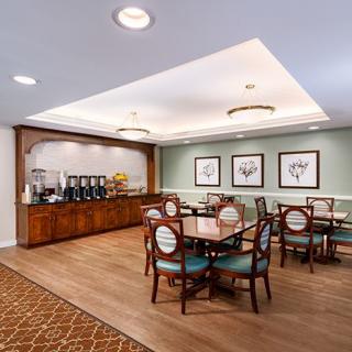 A cozy dining area with wooden tables, chairs, and a coffee station, adorned with framed artwork on the walls.