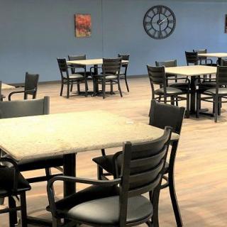 A spacious room with tables and chairs, featuring a wall clock and artwork on blue-painted walls.