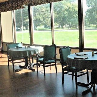 A bright dining area with tables and chairs overlooking a green landscape through large windows.