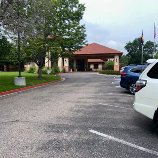 A parking lot leading to a building with several cars parked and trees lining the road.