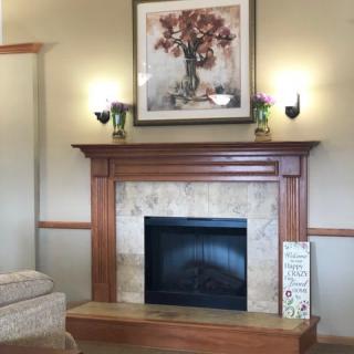 A cozy living room with a wooden fireplace mantel, adorned with a floral painting and wall sconces.