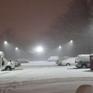 A snowy parking lot illuminated by streetlights during a winter night.